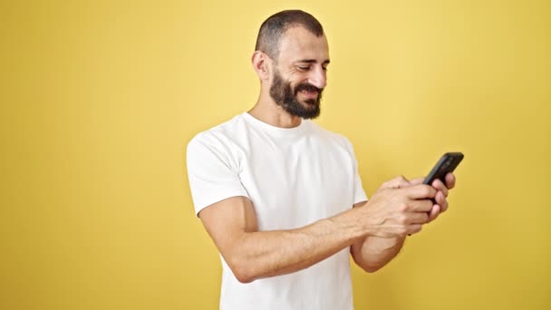 年轻的惊慌失措的男人用智能手机对着孤立的黄色背景微笑 — 图库视频影像