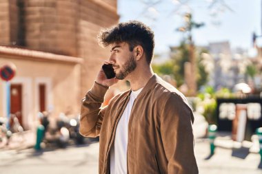 Genç İspanyol adam caddede akıllı telefondan konuşuyor.
