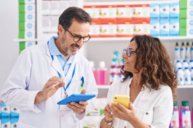 Man and woman pharmacists using touchpad and smartphone working at pharmacy