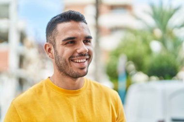 Young hispanic man smiling confident looking to the side at street