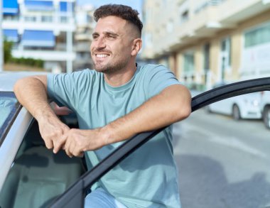 Genç İspanyol adam gülümsüyor. Sokakta araba kapısını açıyor.