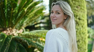 Parkta kendinden emin gülümseyen genç sarışın kadın.