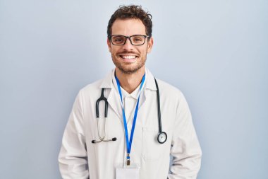 Doktor üniforması giyen genç İspanyol bir adam ve yüzünde mutlu ve havalı bir gülümsemeyle steteskop. şanslı kişi. 