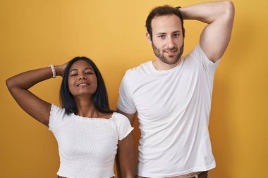 Sarı arka planda duran ırklar arası çift gülümseyerek saçlarına dokunarak el hareketleriyle çekici ve modaya uygun bir poz veriyor. 