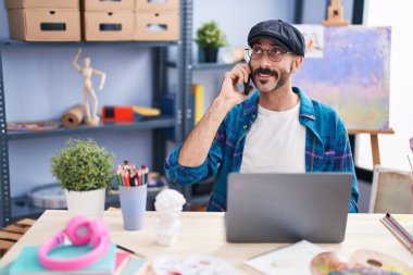 Genç İspanyol ressam dizüstü bilgisayar kullanıyor ve sanat stüdyosunda telefonla konuşuyor.