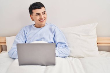 Yatakta dizüstü bilgisayar kullanan genç, ikili olmayan bir adam. 