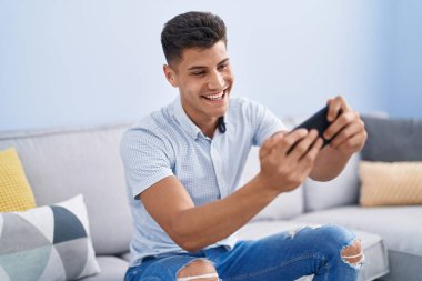 Evdeki kanepede oturan İspanyol asıllı genç oyun oynuyor.