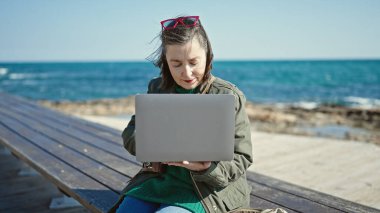 Kır saçlı, laptopunu deniz kenarındaki bankta kullanan olgun İspanyol bir kadın.