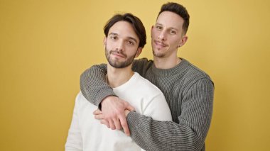 Two men couple hugging each other standing with relaxed expression over isolated yellow background clipart