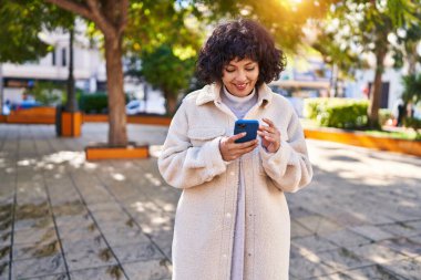 Parkta akıllı telefon kullanarak gülümseyen güzel bir İspanyol kadın.