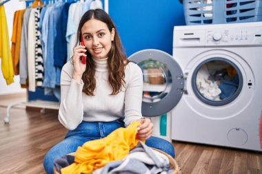 Young beautiful hispanic woman smiling confident talking on smartphone at laundry room