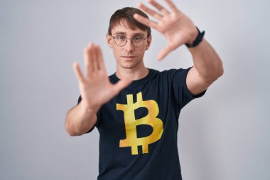 Beyaz, sarışın, bitcoin tişört giyen, el ve parmaklarıyla çerçeve yapan, kamera perspektifi olan bir adam. 