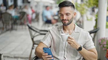 Genç İspanyol adam akıllı telefon kullanıyor. Kahve dükkanının terasında kahve içiyor.