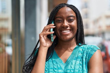 Afro-Amerikalı kadın gülümsüyor. Akıllı telefondan konuşuyor.