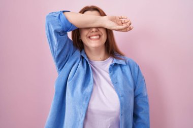 Pembe arka planda duran, gözleri kollarıyla kaplayan, neşeli ve komik gülümseyen İspanyol bir kadın. kör kavram. 