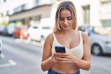 Sokakta akıllı telefon kullanan, kendine güvenen genç sarışın kadın.