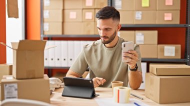 Ofisteki dokunmatik ve akıllı telefonları kullanan Latin asıllı genç bir adam.