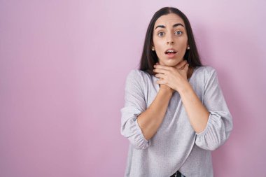 Genç esmer kadın pembe arka planda durup bağırıyor ve boğuluyor çünkü acı verici bir boğulma var. Sağlık problemi. Boğulma ve intihar konsepti. 