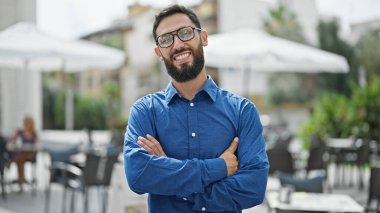 Kahve dükkanının terasında kollarını kavuşturup el kol hareketi yapan genç İspanyol iş adamı.