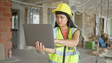 İnşaat alanında dizüstü bilgisayar kullanan Çinli genç bir mimar.