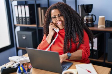 African american woman business worker using laptop talking on telephone at office