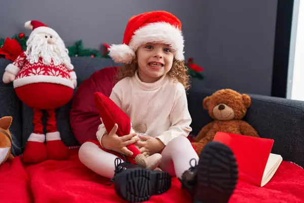 家のクリスマスの装飾によってソファーに座ってサンタクロースの人形を抱擁する愛らしいブロンドの少女 — ストック写真
