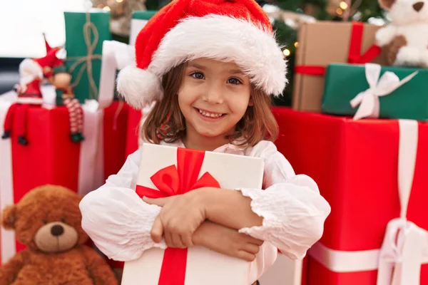 Adorable Hispanic Girl Hugging Christmas Gift Sitting Floor Home — Stock Photo, Image