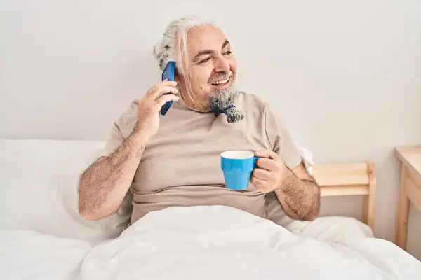 Mężczyzna Średnim Wieku Siwowłosy Rozmawiający Smartfonie Pijący Kawę Sypialni — Zdjęcie stockowe