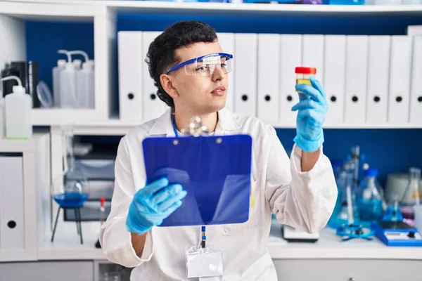 Young non binary man scientist reading report holding urine test tube at laboratory