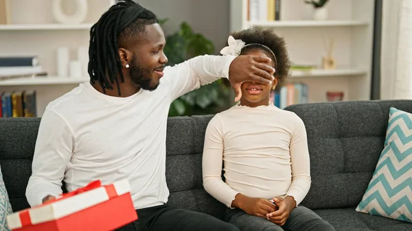 African american father and daughter surprise with gift sitting on sofa smiling at home