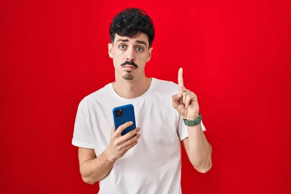 Hispanic Man Using Smartphone Red Background Pointing Looking Sad Upset — Stock Photo, Image