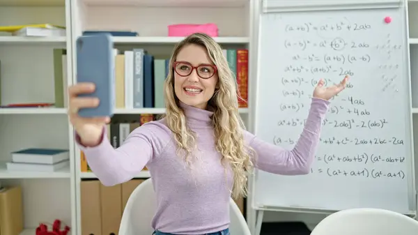 Young blonde woman teacher teaching maths lesson doing video call at classroom