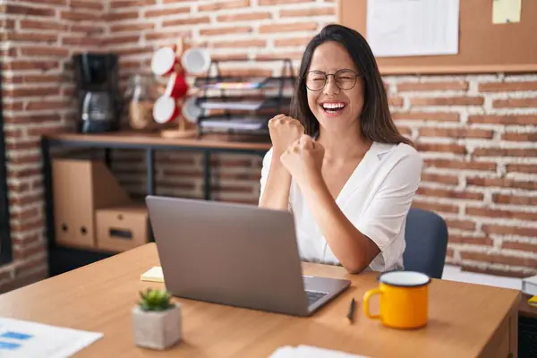 stock image Hispanic young woman working at the office wearing glasses celebrating surprised and amazed for success with arms raised and eyes closed 