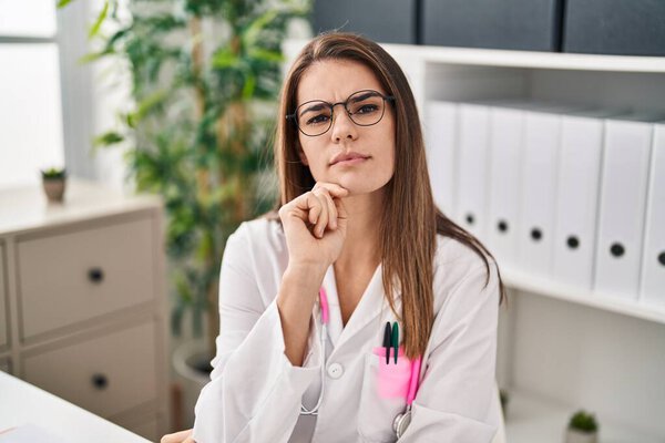 Young beautiful hispanic woman doctor speaking with serious expression at clinic