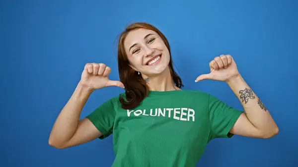 Genç Bir Kadın Mavi Arka Planda Gülümseyen Gönüllü Üniformayı Işaret — Stok fotoğraf