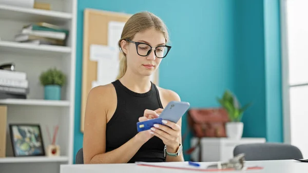 Young blonde woman business worker shopping with smartphone and credit card at the office