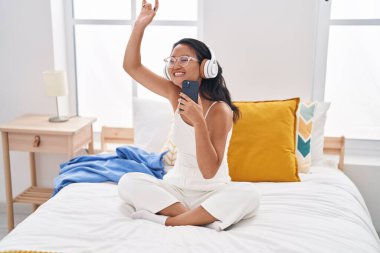Genç Çinli kadın yatak odasında oturmuş müzik dinliyor.