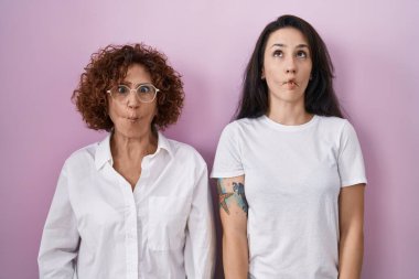 İspanyol anne ve kızı pembe arka plan üzerine gündelik beyaz tişört giyip dudaklı balık suratı yapıyorlar, çılgınca ve komik bir jest. Komik ifade. 