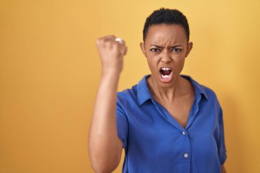 Afrika kökenli Amerikalı bir kadın, öfkeyle bağırırken kızgın ve kızgın bir şekilde yumruğunu kaldırıyor. öfke ve agresif konsept. 