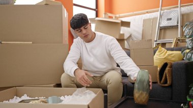 Young hispanic man unpacking cardboard box at new home