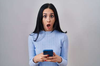 İspanyol kadın şok suratlı akıllı telefon kullanıyor, şüpheci ve alaycı görünüyor, ağzı açık kalınca şaşırıyor. 