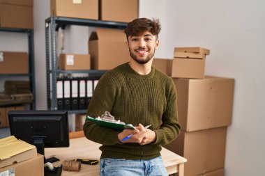 Young arab man ecommerce business worker writing on checklist at office