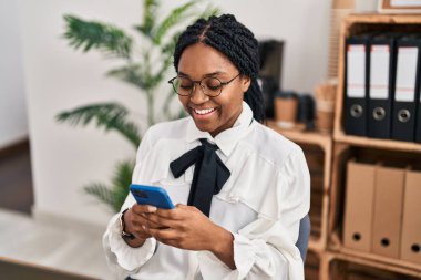 Ofiste dizüstü bilgisayar ve akıllı telefon kullanan Afrikalı Amerikalı iş kadını.