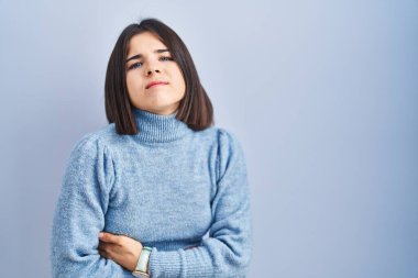 Young hispanic woman standing over blue background with hand on stomach because indigestion, painful illness feeling unwell. ache concept. 
