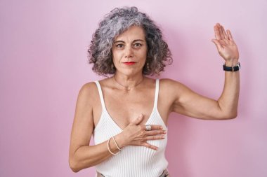 Pembe arka planda duran gri saçlı orta yaşlı bir kadın. Göğüs ve avuç içi açık küfür ediyor. Sadakat yemini ediyor. 