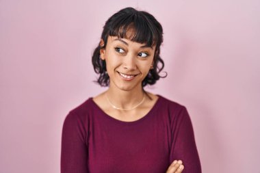 Young beautiful woman standing over pink background smiling looking to the side and staring away thinking. 