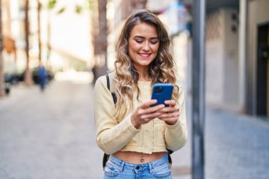 Young woman tourist smiling confident using smartphone at street
