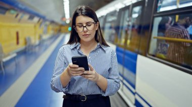Madrid metro istasyonunda akıllı telefon kullanan güzel İspanyol bir kadın metroda bekliyor.
