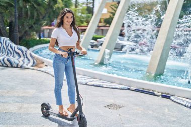 Young hispanic woman smiling confident using e-scooter at park