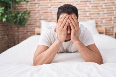 Young hispanic man stressed lying on bed at bedroom